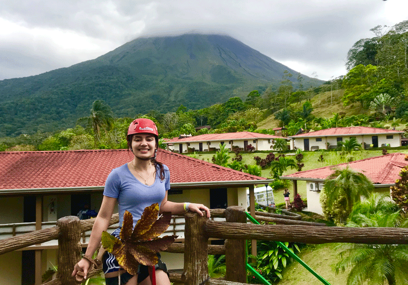 Girl dressed in zipline gear with houses and volcano in the background